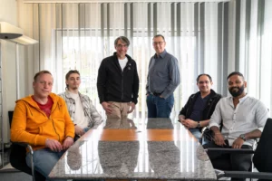 Das Team der DT Netsolution sitzt um einen Tisch und schaut in die Kamera.