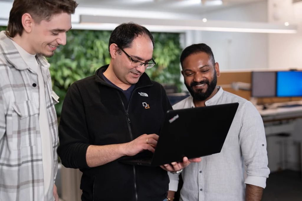 Ein Mitarbeiter zeigt seinen beiden Kollegen etwas auf einem Laptop.