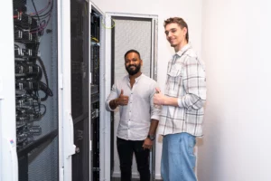 Zwei Mitarbeiter der DT Netsolution schauen in die Kamera und zeigen "Daumen hoch".