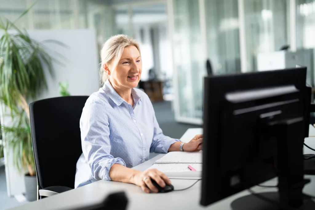 Eine Frau sitzt an der Rezeption und arbeitet an einem PC.